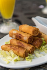 Some spring rolls stacked on each other in a salad bed. Drink in the background.