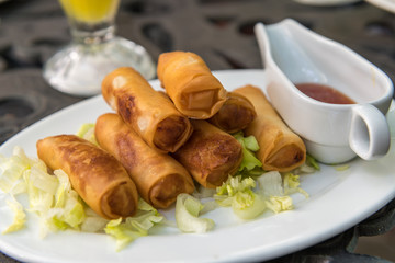 Spring roll prepared on a plate, with salad and sauce.