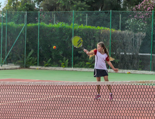 Girl tennis player, playing in the open air. Young girl playing tennis on court