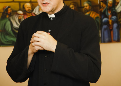Priest in black cassock with clerical collar prays
