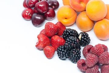 heaps of assorted summer fruits of cherries strawberries apricots blackberries and raspberry on white with copy space
