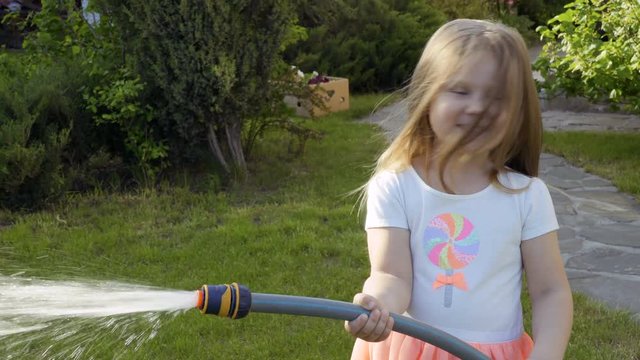 Little girl water a flower bed from a hose