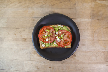 Avocado toast with sliced tomatoes and green onions on multigrain toast. Served on a wooden platform.