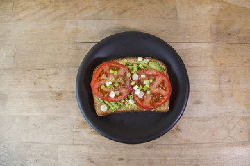 Avocado toast with sliced tomatoes and green onions on multigrain toast. Served on a wooden platform.