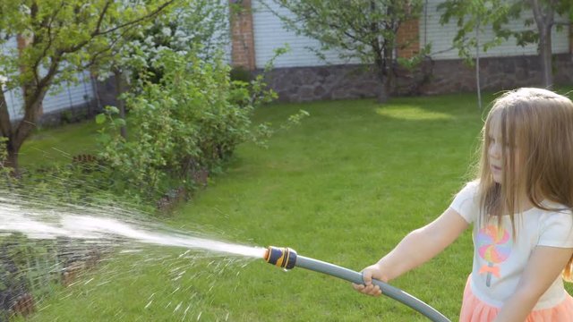 Cute little girl water a flower bed from a hose