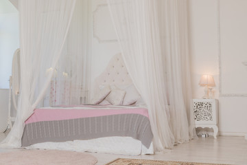 Bedroom in soft light colors with a wooden floor. Big comfortable four poster double bed in elegant classic bedroom. Natural white with wood interior design.Large bed.