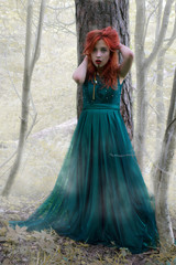 Crazy girl with red hair in green dress in mysterious forest