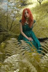 Crazy girl with red hair in green dress in mysterious forest