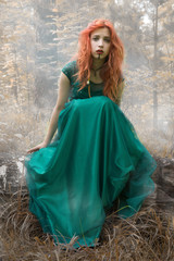 Crazy girl with red hair in green dress in mysterious forest