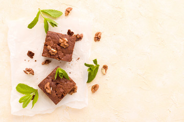 Brownie sweet chocolate dessert with walnuts and meant leaves on white paper with copy space on pastel beige background.