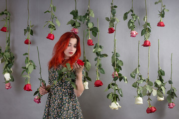 Girl with red hair among hanging roses