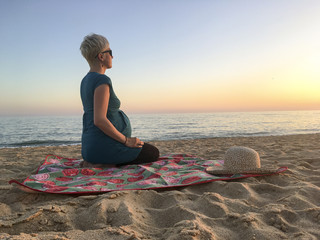 Fototapeta na wymiar Woman in ninth month of pregnancy looking toward sunset on the beach