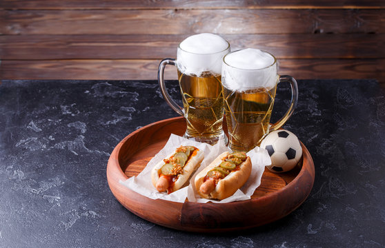 Photo of two glasses of beer and hot dogs on wooden tray with football