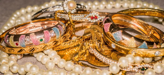 stack of jewelry, gold bracelet, pearl necklace, and colorful gemstone. wealth and investment...