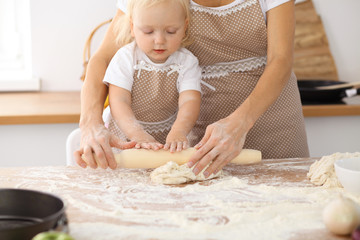 Little girl and her blonde mom in beige aprons  playing and laughing while kneading the dough in the kitchen. Homemade pastry for bread, pizza or bake cookies