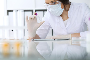 Close-up of professional female scientist in protective eyeglasses making experiment with reagents in laboratory. Medicine and research concept