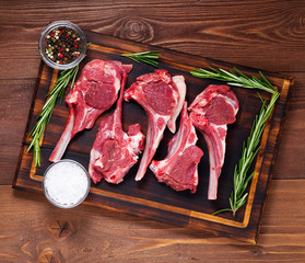 Raw lamb cutlets on bone on dark brown wooden background, lamb ribs, top view.