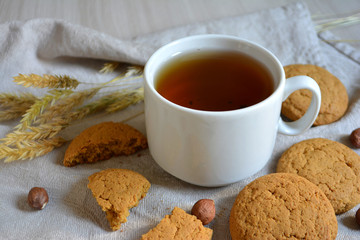 Tea in a cup, oatmeal cookies and nuts on the table