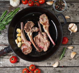Roasted lamb ribs with rosemary, tomatoes and garlic on pan on dark old rustic wooden background, top view