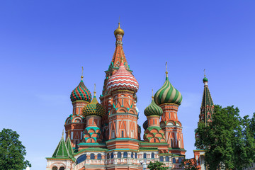 Domes of St. Basil's Cathedral against green trees and blue sky on a sunny summer morning