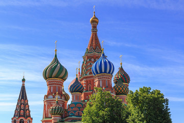 Fototapeta na wymiar Domes of St. Basil's Cathedral on Red square in Moscow against green trees on a sunny summer morning