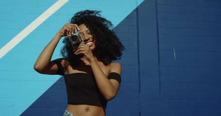 Beautiful young woman shooting photos with film camera against colorful blue wall - Powered by Adobe