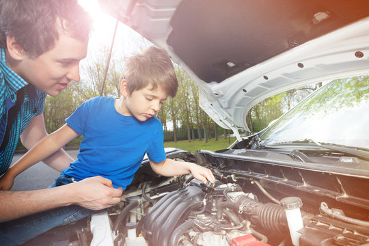 Little boy watching his father work on car engine