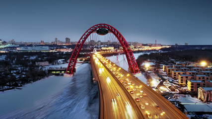 Flying around the Picturesque Bridge over the Moskva river at dusk. Aerial dolly shot of the intense traffic on the illuminated bridge over the frozen river.