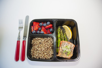 Meal planning. Salmon with asparagus, quinoa, and fruit in a food prep container.