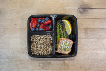 Meal planning. Salmon with asparagus, quinoa, and fruit in a food prep container.