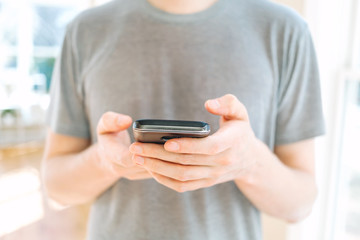 Man's hands using a smartphone on a bright interior background
