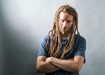 Man with dreadlocks with arms folded on a dark background