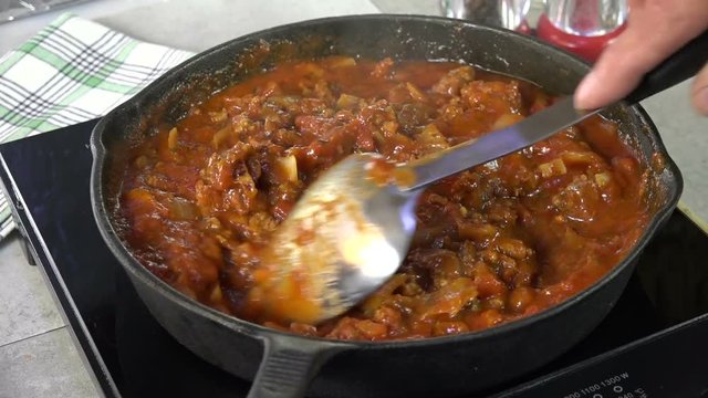 Stirring spaghetti sauce with meat in a cast iron skillet
