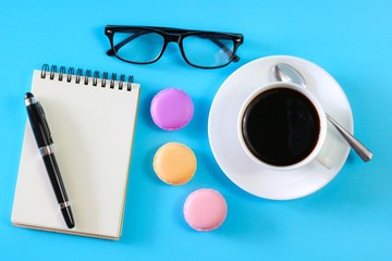 Flat lay photo with notebook , coffee cup Pen, glasses and Macaroon on blue background