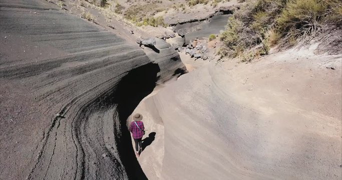 Aerial view of female hiker walking in a magma rock formed by a water river. Magma rocks wavy forms. 4k