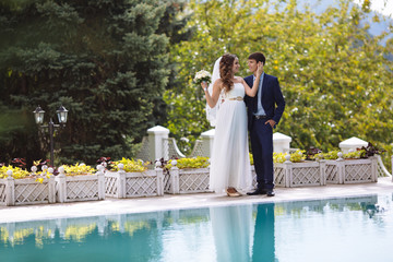 A girl in a wedding light dress is holding a bouquet of flowers, and gently touches the face of the man, dressed in a business suit. Wedding concept.