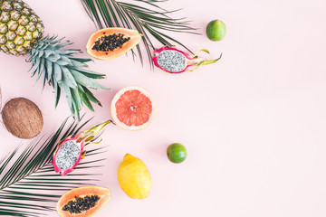 Summer fruits. Tropical palm leaves, pineapple, coconut, papaya, dragon fruit, orange on pastel pink background. Flat lay, top view, copy space