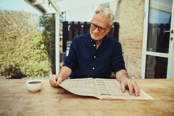 Senior man relaxing outside with a coffee and newspaper
