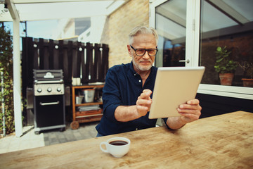 Smiling senior man using a digital tablet and drinking coffee