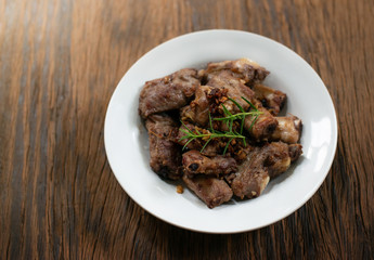 Fried pork spare ribs with garlic and pepper in whit plate on wooden table, rosemary on top