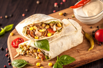 Burritos, kebab, shaurma wraps beef and vegetables on a black background and lies on a wooden...