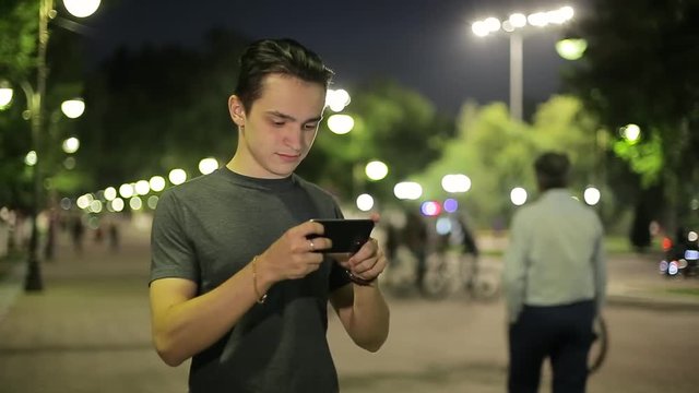 Man sms texting using app on smart phone at night in city. Handsome young business man using smartphone smiling happy. A warm summer evening.