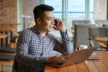 Young businessman talking on phone and using laptop for work