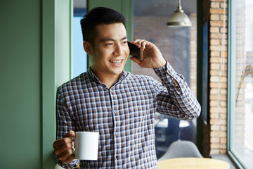 Young man using his telephone while drinking coffee at cafe