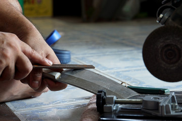 Hand of man use old metal file sharpening big knife in house with blurred floor background.