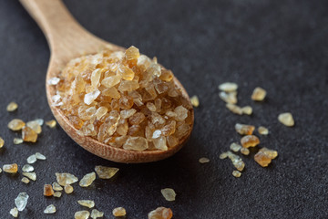 Natural brown sugar or no bleach sugar on wood spoon on black granite table in close up view macro concept with copy space. Sweet seasoning for good health. Ingredient prepared for cooking or bakery.