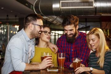 Group of four friends drinking beer in pub