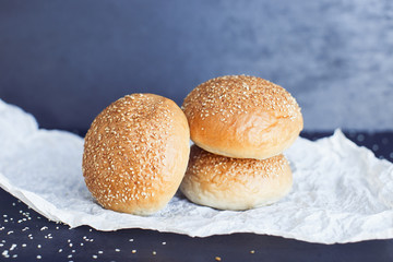 Three fresh buns on the butter-paper on the black background