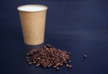 Cappuccino in brown paper cup with coffee beans on the black background