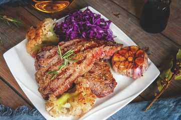 Steak rare with the blood of vegetables tomatoes and spinach grilled in a white plate at home on a light background. Close up.